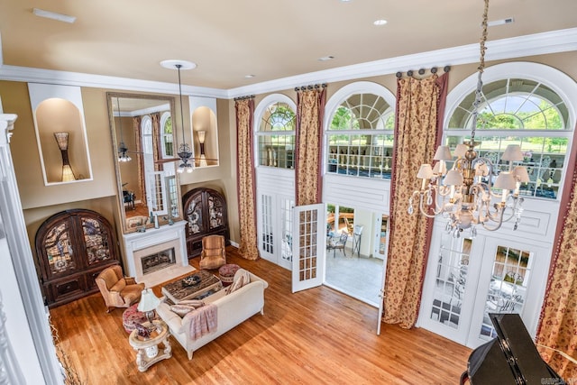 living area featuring wood finished floors, crown molding, french doors, a fireplace, and ceiling fan with notable chandelier