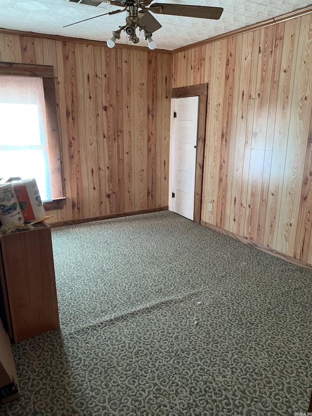 carpeted empty room with crown molding, ceiling fan, and wooden walls