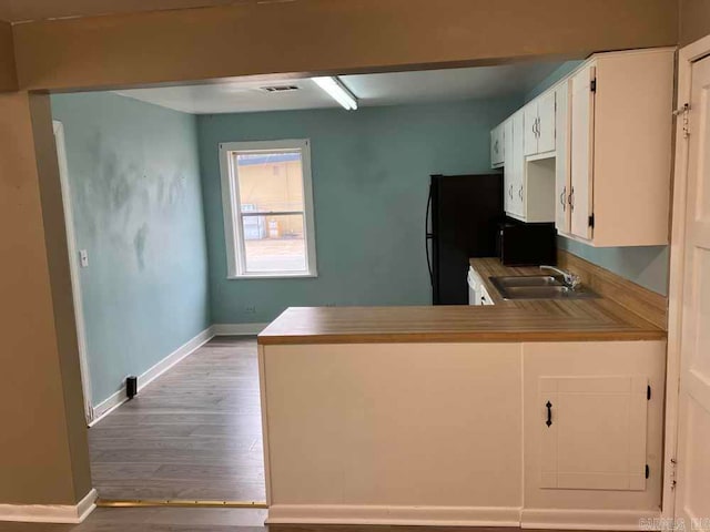 kitchen with white cabinetry, black refrigerator, kitchen peninsula, sink, and light hardwood / wood-style floors