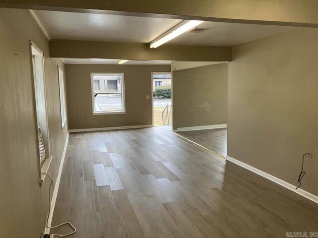 empty room featuring beamed ceiling and wood-type flooring