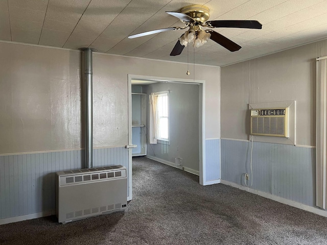 unfurnished living room featuring carpet, a wainscoted wall, a wall unit AC, radiator heating unit, and a ceiling fan