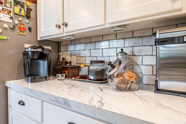 kitchen featuring light stone countertops, stainless steel fridge, decorative backsplash, and white cabinetry