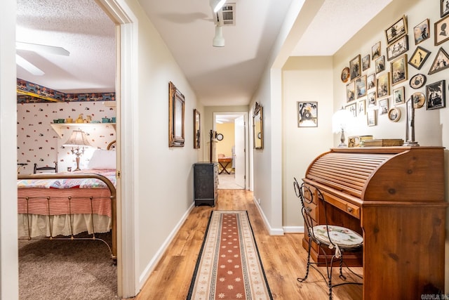 hallway with a textured ceiling and light hardwood / wood-style flooring