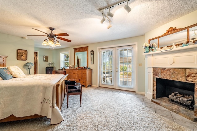 bedroom featuring light carpet, a textured ceiling, rail lighting, a tile fireplace, and ceiling fan