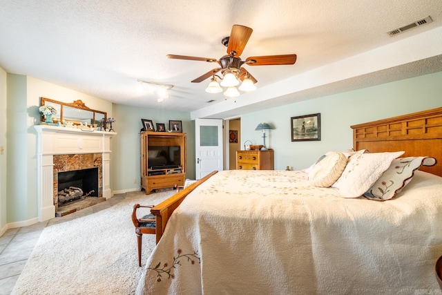 tiled bedroom with ceiling fan, a fireplace, and a textured ceiling