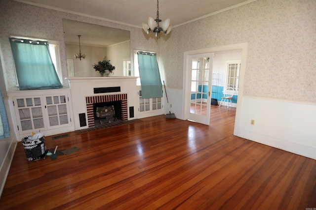 unfurnished living room with a fireplace, a healthy amount of sunlight, crown molding, wood-type flooring, and an inviting chandelier