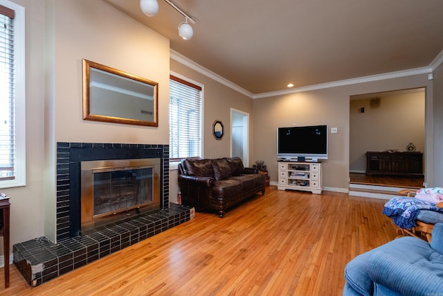 living room featuring track lighting, hardwood / wood-style flooring, a tiled fireplace, and ornamental molding