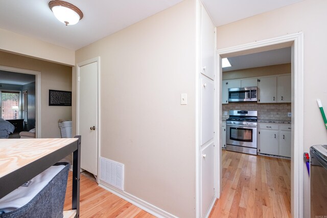 interior space featuring light wood-type flooring, appliances with stainless steel finishes, and decorative backsplash