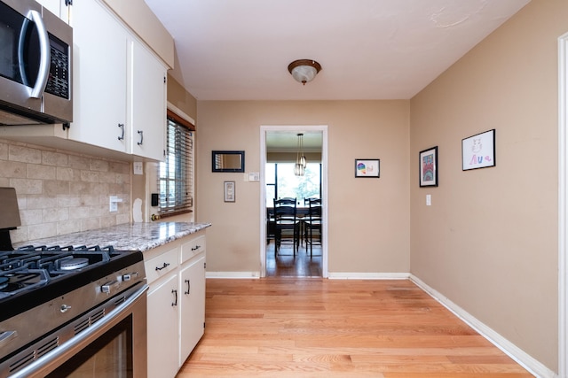 kitchen featuring white cabinets, appliances with stainless steel finishes, light stone countertops, light hardwood / wood-style floors, and tasteful backsplash