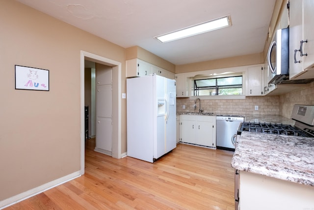 kitchen with light wood-type flooring, appliances with stainless steel finishes, white cabinetry, and light stone counters