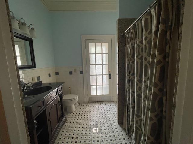 bathroom with a wainscoted wall, toilet, curtained shower, tile walls, and vanity