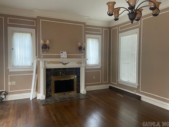 unfurnished living room featuring wood finished floors, a high end fireplace, ornamental molding, a decorative wall, and a wealth of natural light