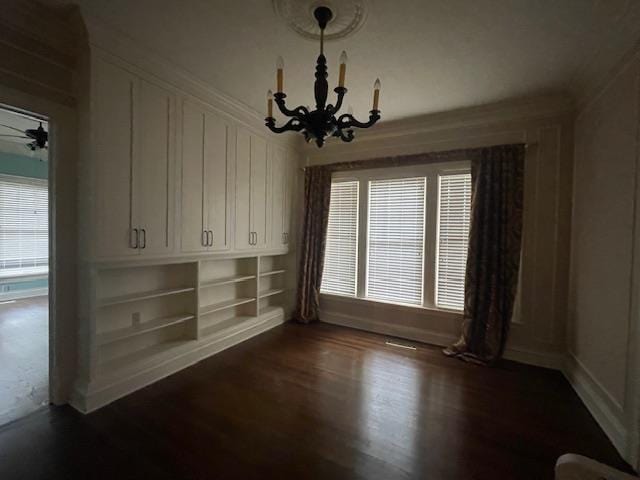 unfurnished dining area featuring dark wood-style floors, built in features, and an inviting chandelier