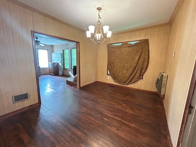 spare room featuring ceiling fan with notable chandelier, wood walls, dark hardwood / wood-style flooring, and heating unit