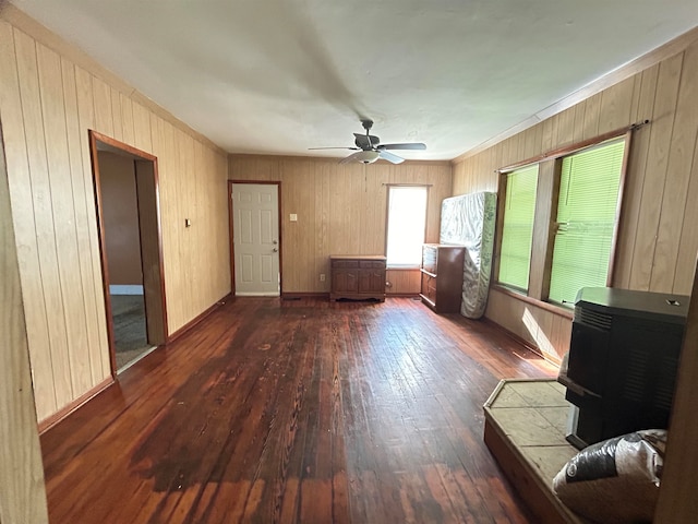 unfurnished living room with a wood stove, wood walls, ceiling fan, and dark wood-type flooring