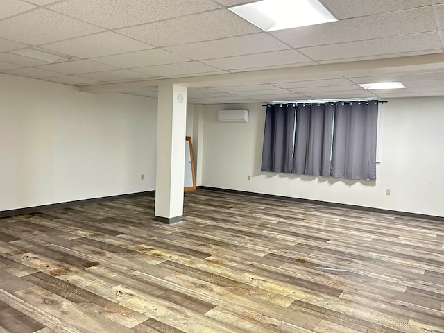 basement with wood-type flooring, a wall mounted air conditioner, and a paneled ceiling