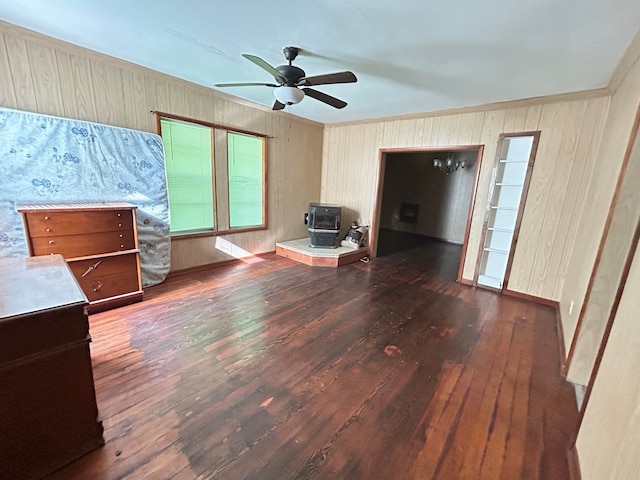 unfurnished living room with wooden walls, dark hardwood / wood-style flooring, ceiling fan, and a wood stove