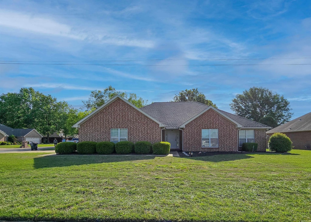 ranch-style home featuring brick siding, roof with shingles, and a front yard