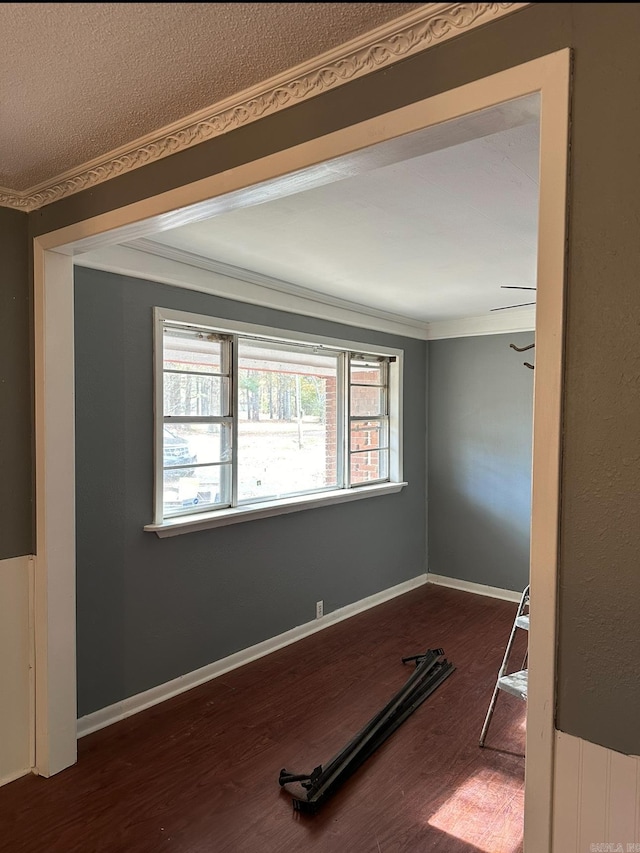 empty room featuring crown molding, dark wood finished floors, and baseboards