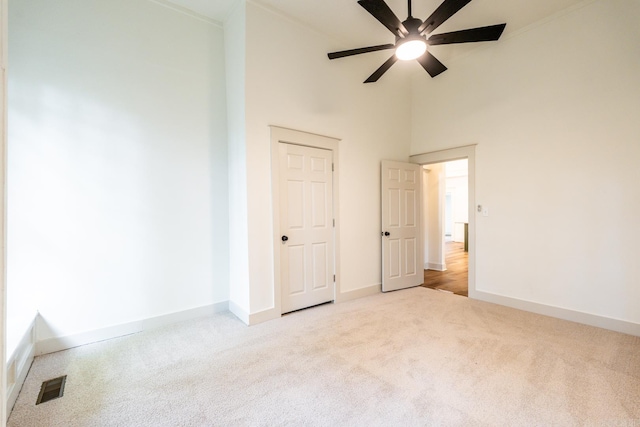 unfurnished bedroom featuring light carpet, a towering ceiling, and ceiling fan