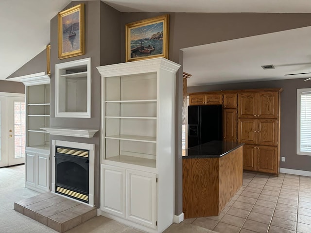 kitchen with black refrigerator with ice dispenser, vaulted ceiling, light tile patterned flooring, a fireplace, and french doors