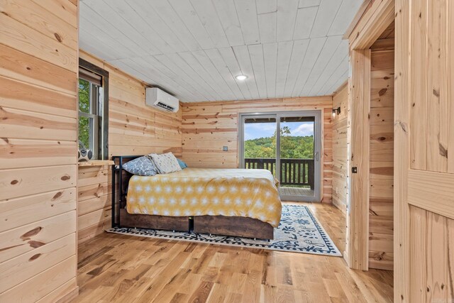 bedroom featuring an AC wall unit, hardwood / wood-style floors, multiple windows, and access to outside