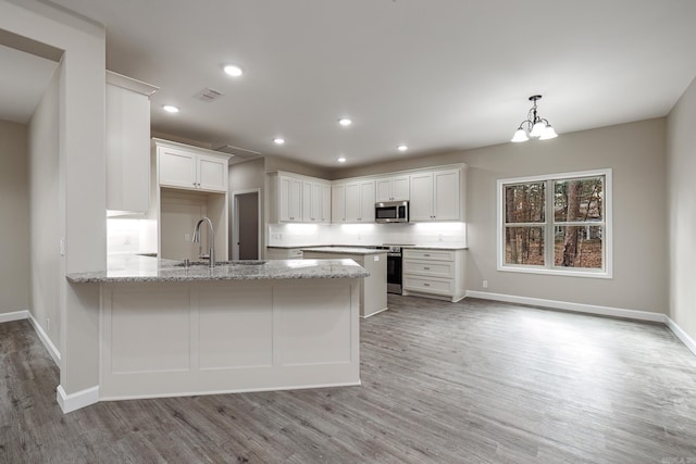 kitchen with light stone countertops, appliances with stainless steel finishes, a peninsula, and white cabinetry