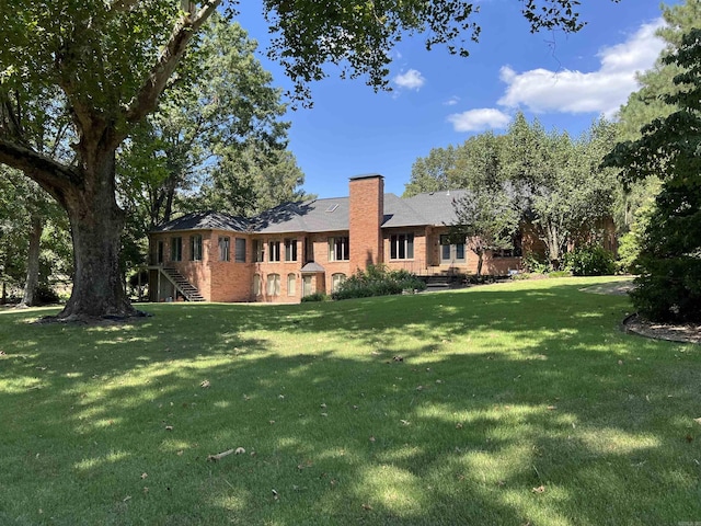 rear view of property featuring stairs, a lawn, brick siding, and a chimney