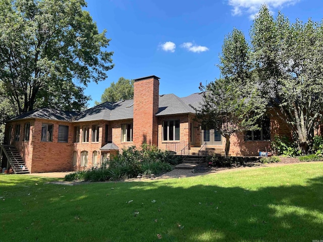 rear view of house with brick siding, a lawn, and a chimney