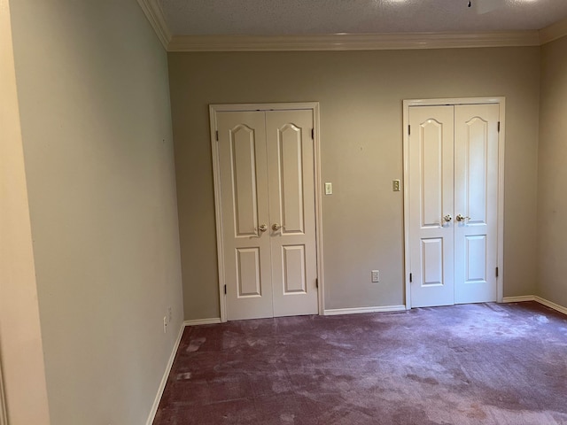 unfurnished bedroom featuring a textured ceiling, crown molding, carpet flooring, and multiple closets