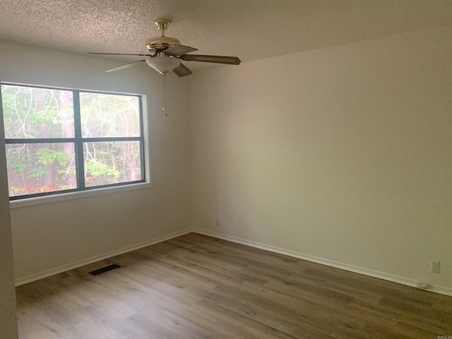 empty room featuring visible vents, a textured ceiling, baseboards, and wood finished floors