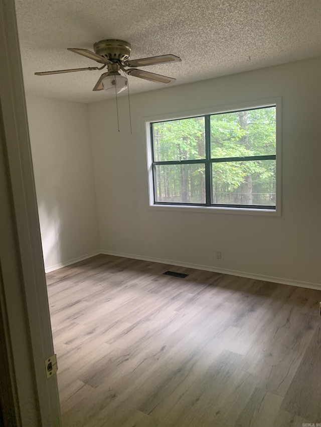 unfurnished room with visible vents, a textured ceiling, baseboards, and wood finished floors