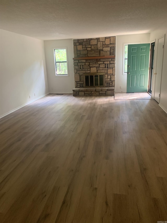 unfurnished living room with baseboards, a stone fireplace, a textured ceiling, and wood finished floors