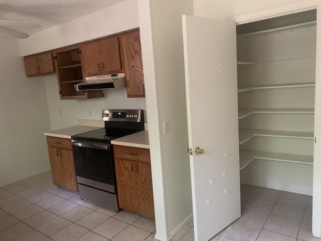 kitchen with light tile patterned floors, brown cabinets, light countertops, stainless steel range with electric cooktop, and under cabinet range hood