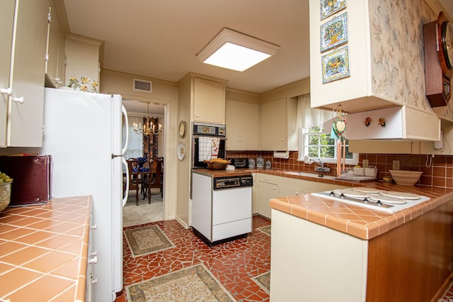 kitchen featuring an inviting chandelier, dark tile patterned floors, white appliances, tile countertops, and kitchen peninsula