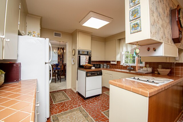 kitchen with white appliances, tasteful backsplash, visible vents, tile counters, and an inviting chandelier