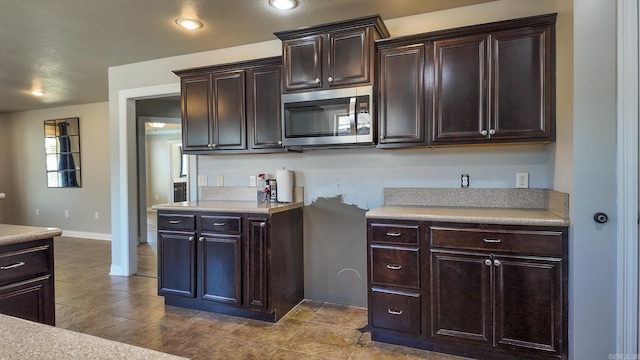 kitchen with stainless steel microwave, light countertops, dark brown cabinets, and recessed lighting