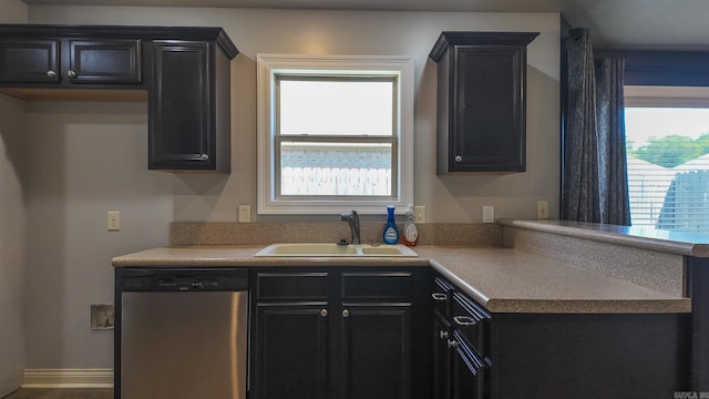 kitchen with dark cabinets, a peninsula, light countertops, stainless steel dishwasher, and a sink