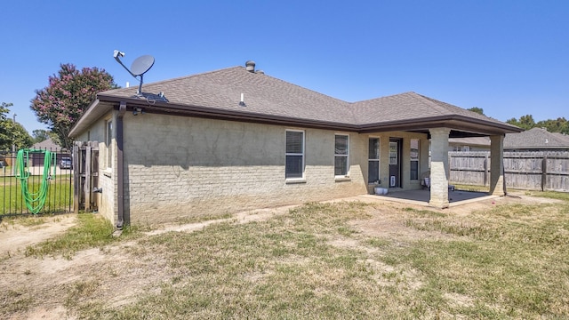 rear view of house featuring roof with shingles, fence, a yard, a patio area, and stucco siding