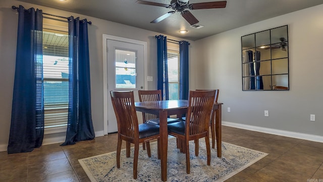 dining space with a ceiling fan, dark tile patterned flooring, visible vents, and baseboards