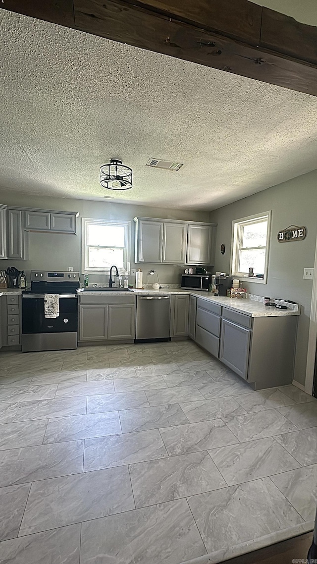 kitchen featuring appliances with stainless steel finishes, light countertops, a sink, and gray cabinetry