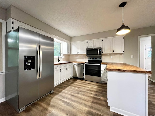 kitchen featuring stainless steel appliances, wood-type flooring, kitchen peninsula, sink, and white cabinets