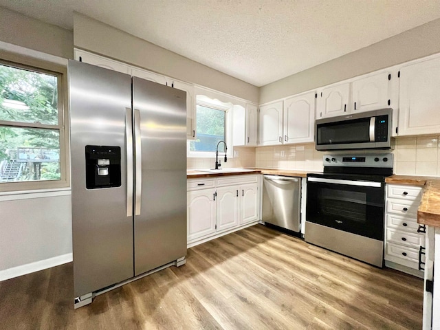 kitchen with a wealth of natural light, wood counters, stainless steel appliances, and white cabinets