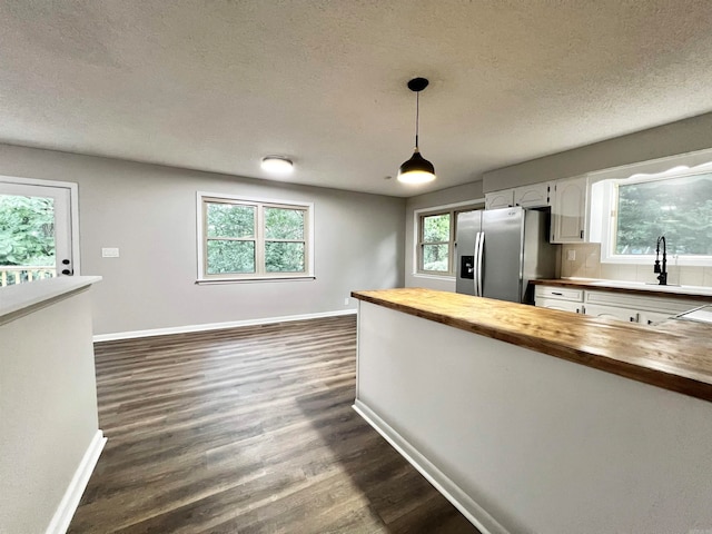 kitchen featuring a textured ceiling, dark hardwood / wood-style floors, butcher block countertops, pendant lighting, and stainless steel fridge with ice dispenser