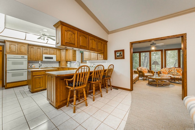 kitchen featuring a breakfast bar area, white appliances, kitchen peninsula, lofted ceiling, and ceiling fan