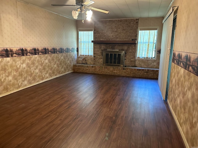 unfurnished living room with plenty of natural light, ceiling fan, a brick fireplace, and dark hardwood / wood-style flooring