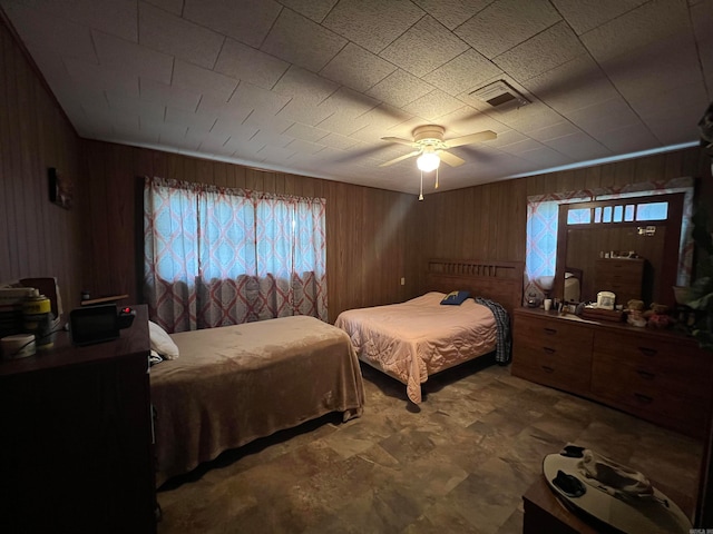 bedroom featuring ceiling fan, wood walls, and multiple windows