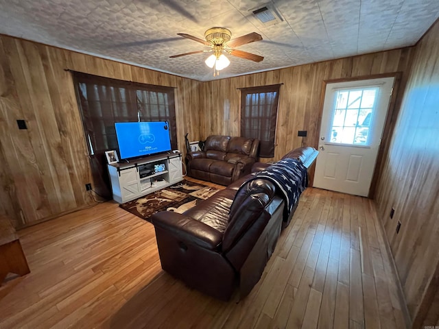 living room with ceiling fan, wooden walls, and wood-type flooring