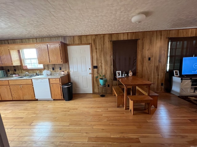 kitchen featuring dishwasher, wood walls, sink, and light hardwood / wood-style floors