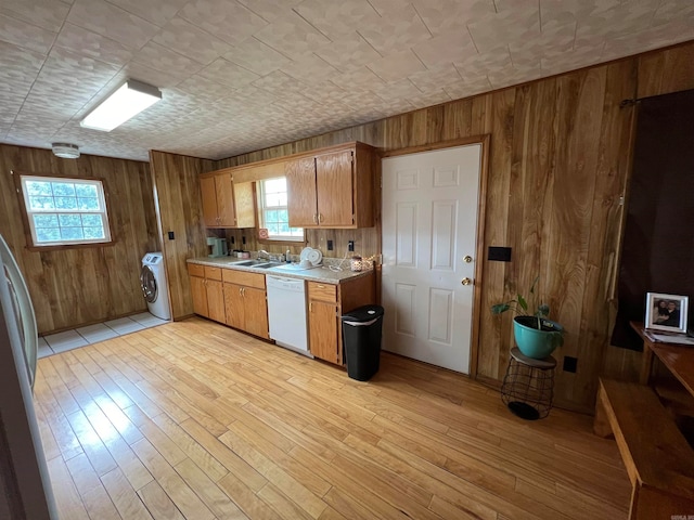 kitchen featuring white dishwasher, light hardwood / wood-style flooring, washer / dryer, and wooden walls